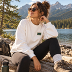 Woman wearing the white WILD crewneck outdoors by a mountain lake