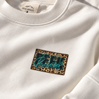 Close-up of the leopard-print Peek Breeze logo on the white WILD crewneck
