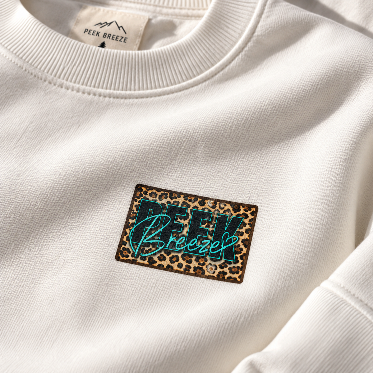 Close-up of the leopard-print Peek Breeze logo on the white WILD crewneck