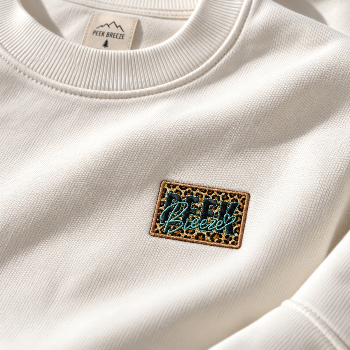 Close-up of the embroidered leopard Peek Breeze logo on the WILD crewneck