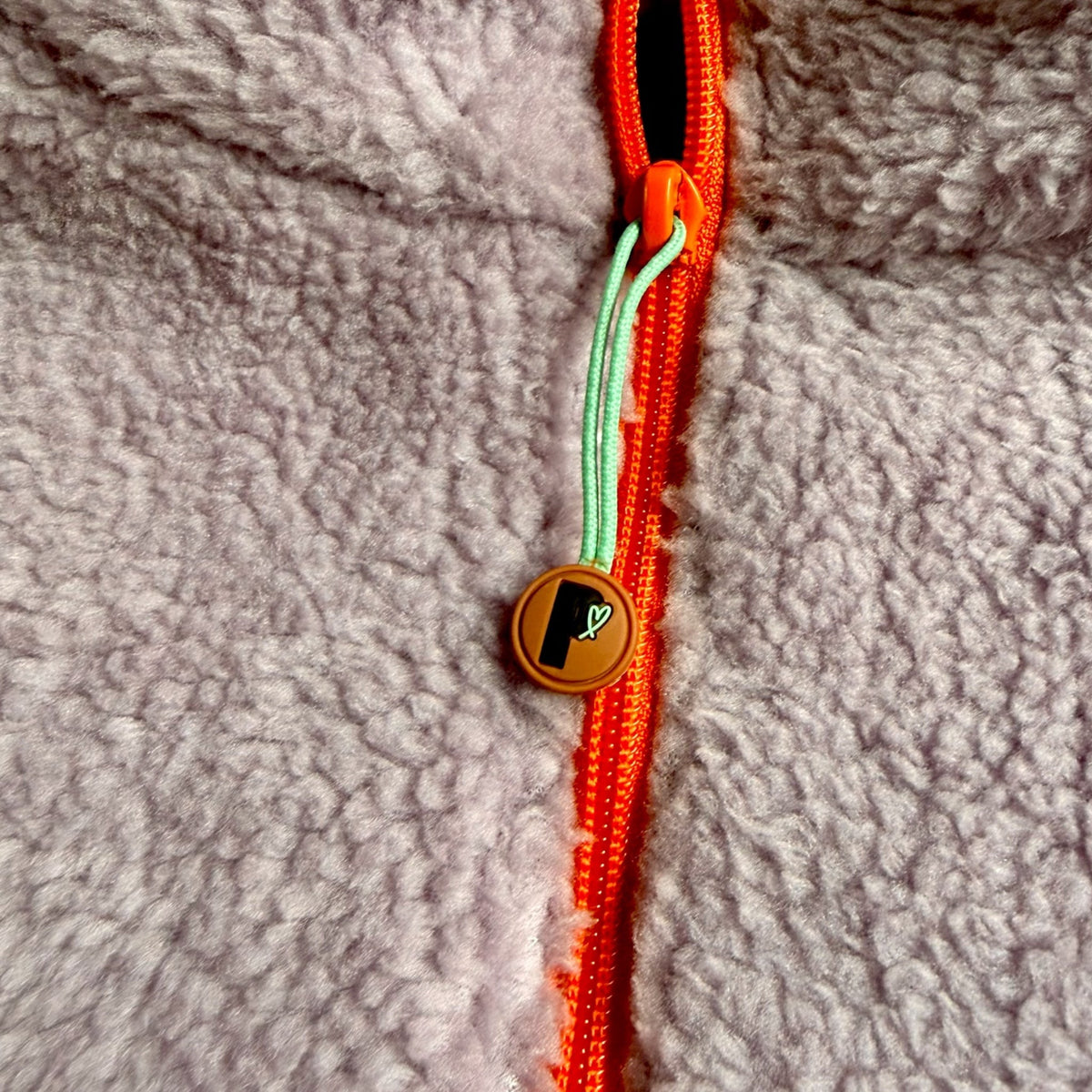 Close-up of the lavender sherpa with orange zipper and turquoise logo pull on the Aspen dress