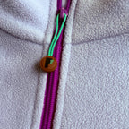 Close-up of the fuchsia quarter-zip and Peek Breeze logo zipper pull on lilac fleece