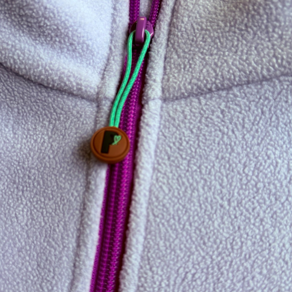 Close-up of the fuchsia quarter-zip and Peek Breeze logo zipper pull on lilac fleece