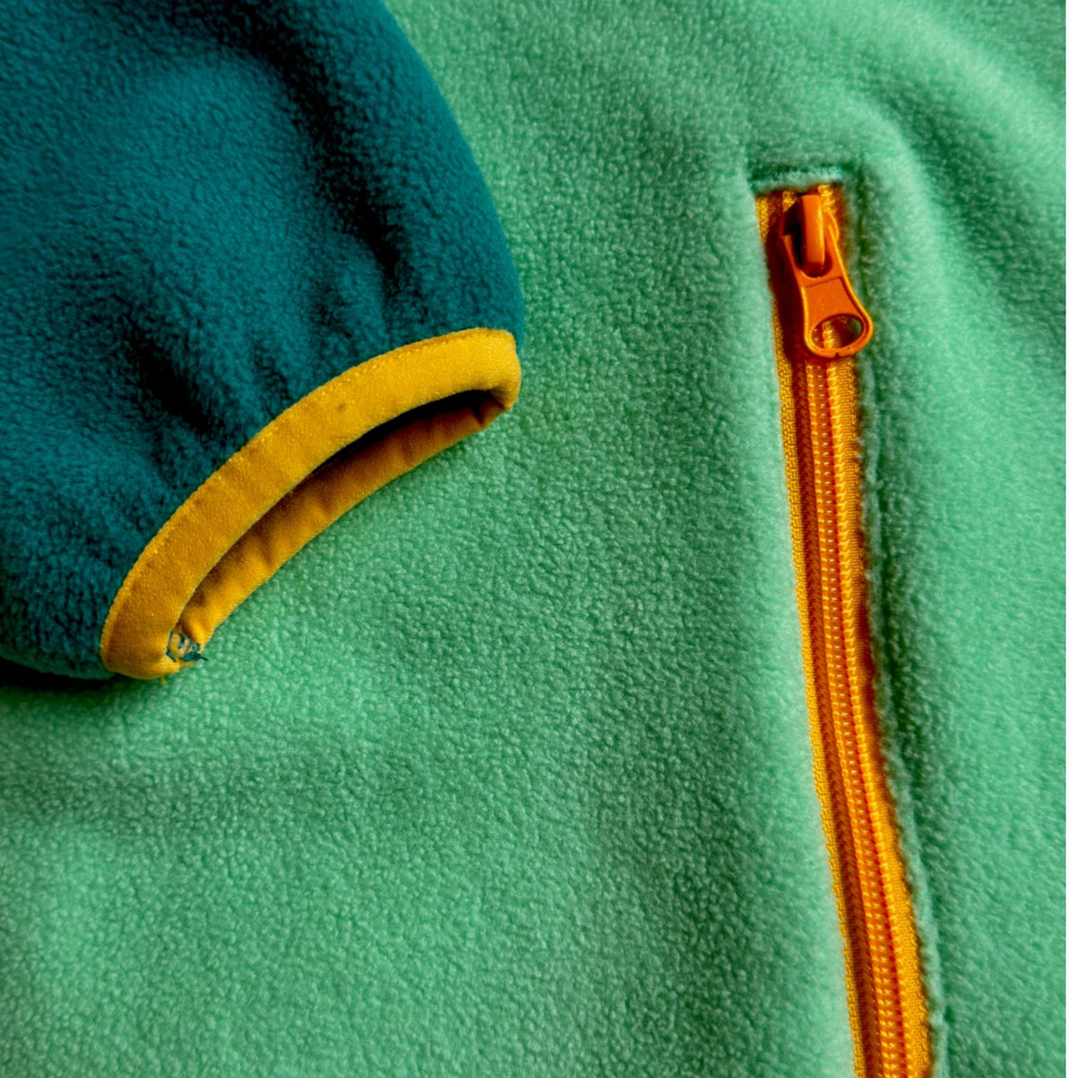 Close-up of the yellow cuff trim and zippered side pocket on the mint fleece