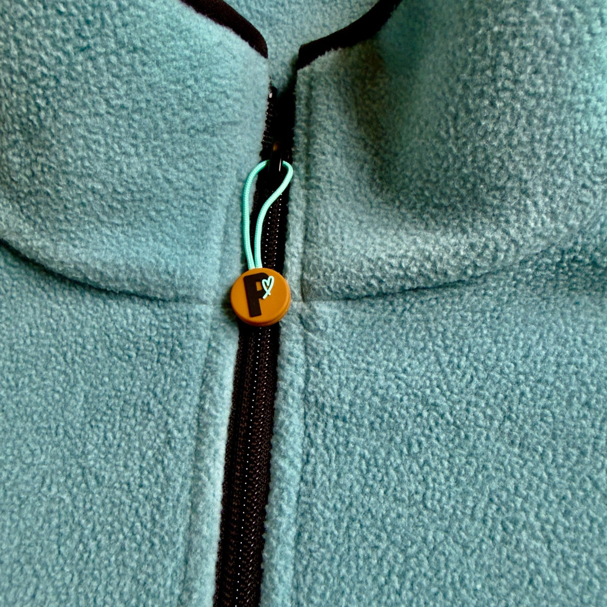 Close-up of the black quarter-zip and Peek Breeze logo zipper pull on sage green fleece