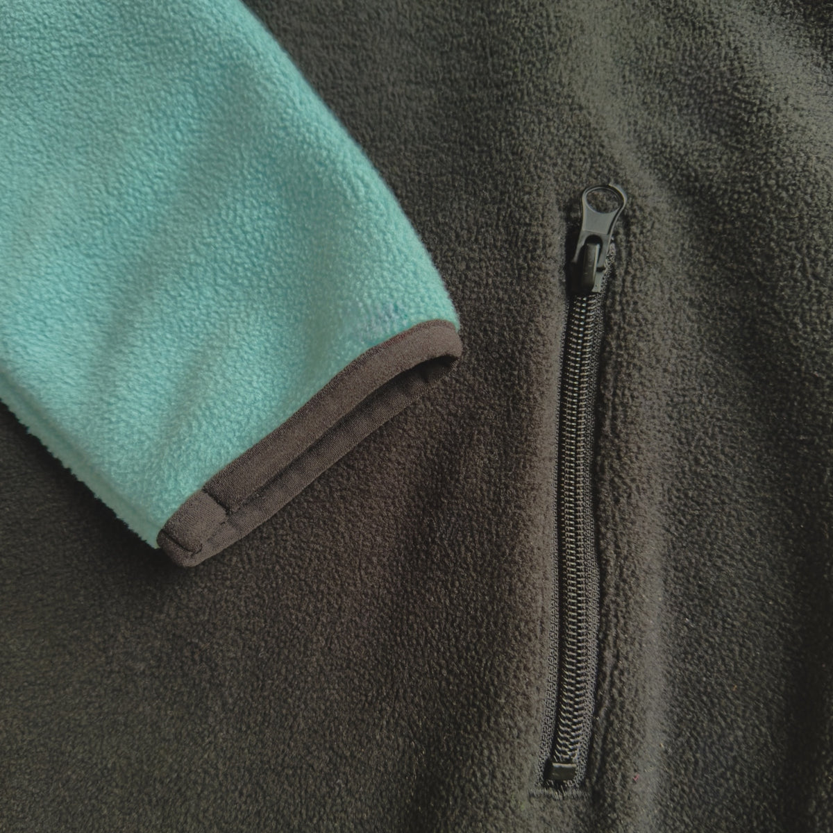 Close-up of the sage sleeve with black cuff trim and zippered side pocket on the black fleece