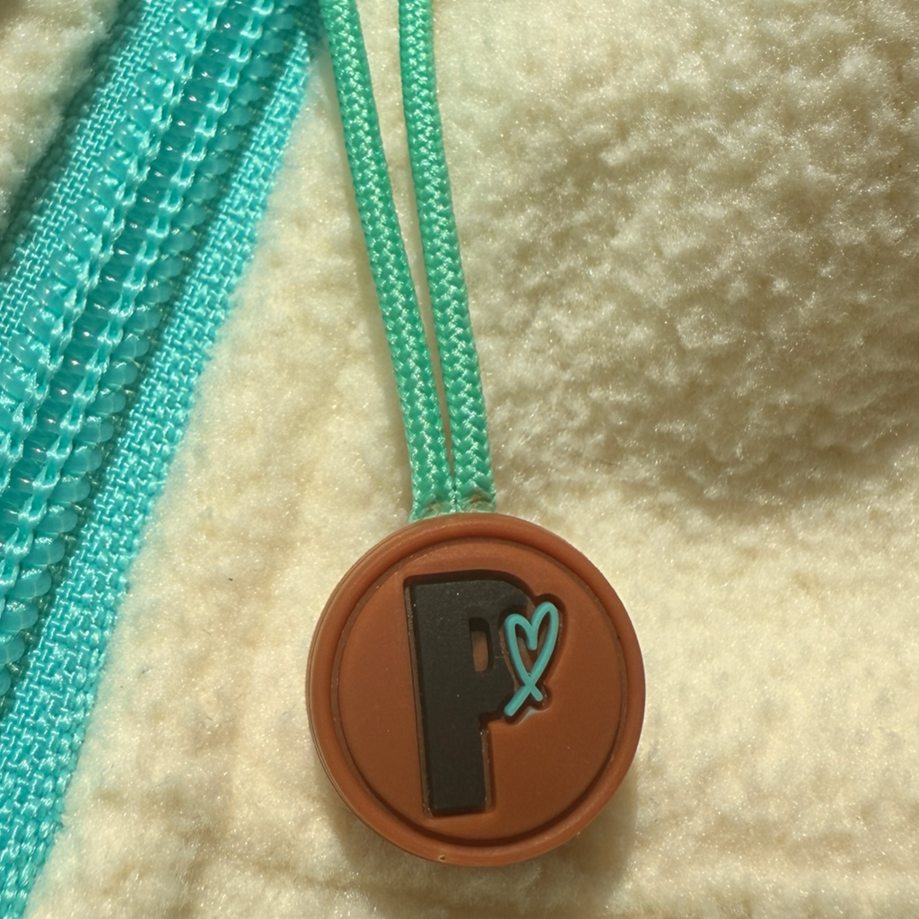 Close-up of the Peek Breeze Oasis fleece dress featuring the signature turquoise zipper pull and round brown branded charm.