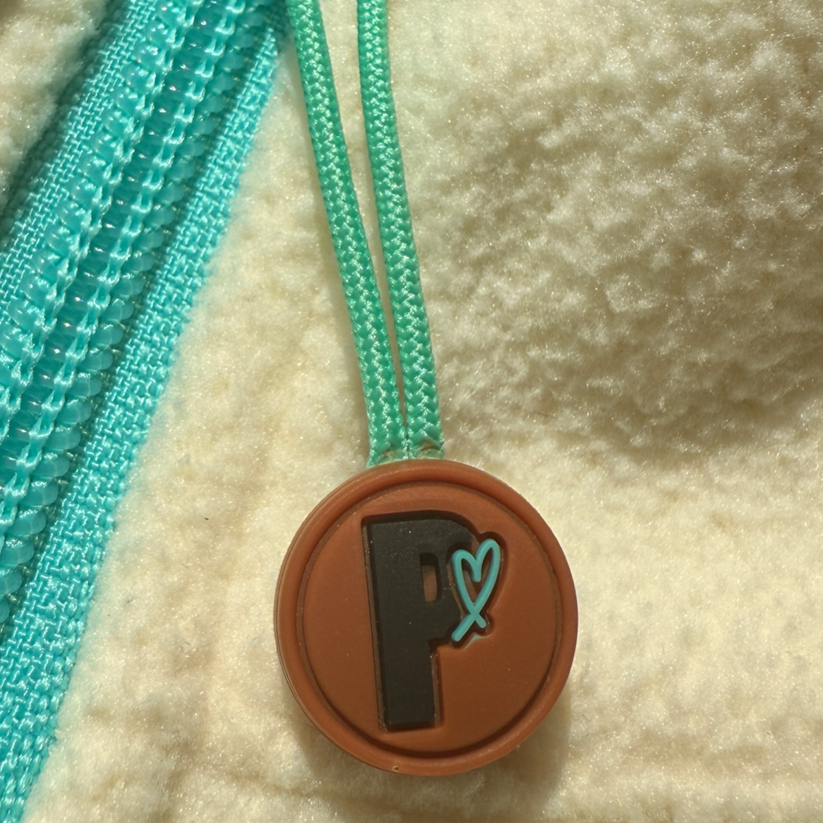 Close-up of the Peek Breeze Oasis fleece dress featuring the signature turquoise zipper pull and round brown branded charm.