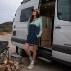 Woman wearing the Seaside hooded fleece dress in light blue and navy next to a camper van