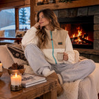 Woman wearing the Oasis beige and ivory vest by the fireplace at the cabin